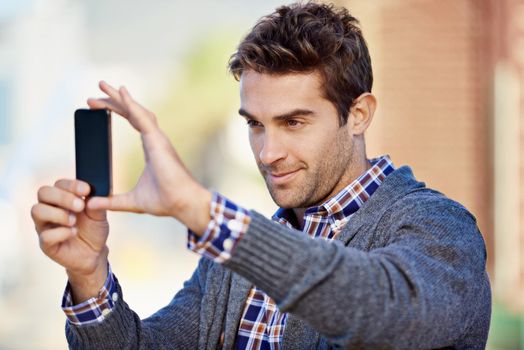 Phone photography. Shot of a handsome young man taking a photograph with his mobile phone phone outdoors.