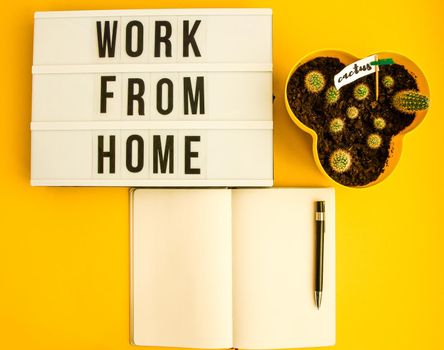 lightbox with text WORK FROM HOME with notebook pen and cactus and TO DO list, copy space on yellow background, quarantine and isolation HOME OFFICE
