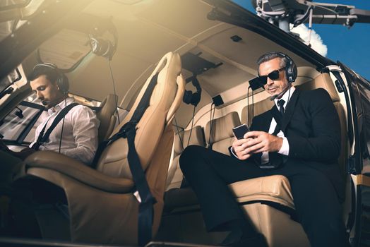 Premium business requires premium transport. Shot of a mature businessman using a mobile phone while traveling in a helicopter.