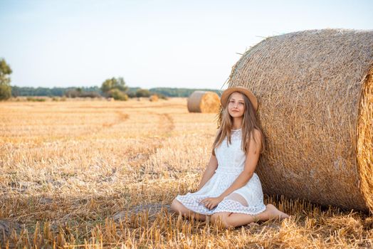 Barefoot girl near the bale of straw in the agricultural field