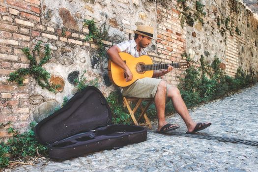 Granada / Spain - August 21 2019: A male busker sitting playing the Spanish acoustic guitar in an alleyway