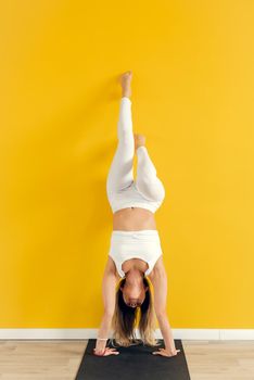 Yogini practicing yoga pose in the gym. The woman stands upside down