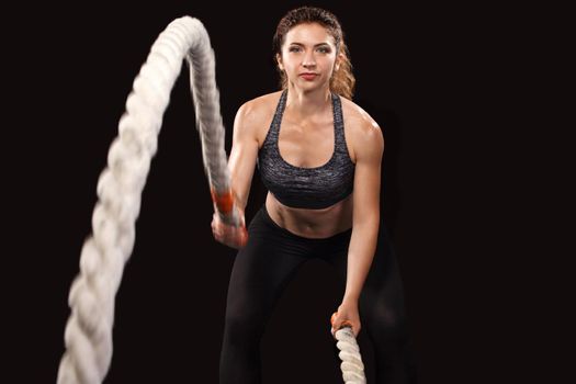 Battle ropes session. Attractive young fit and toned sportswoman working out in functional training gym doing exercise with battle ropes. Fitness and workout motivation