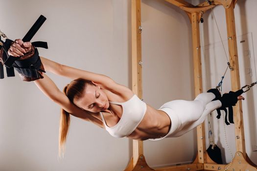 A girl in a sports uniform does exercises on a simulator for stretching the human body