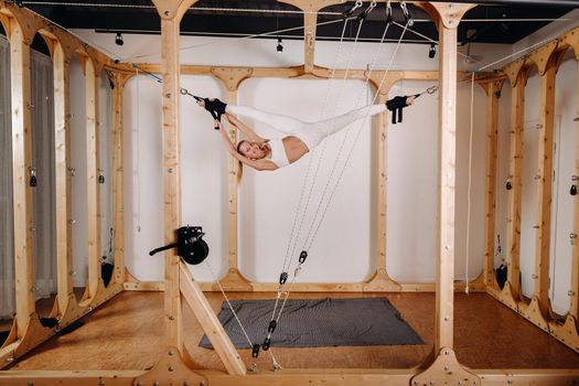 A girl in a sports uniform does exercises on a simulator for stretching the human body
