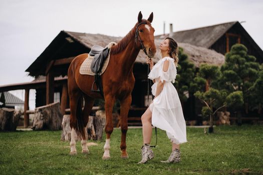Beautiful girl in a white sundress next to a horse on an old ranch