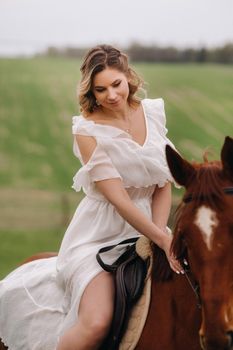 A woman in a white sundress riding a horse in a field