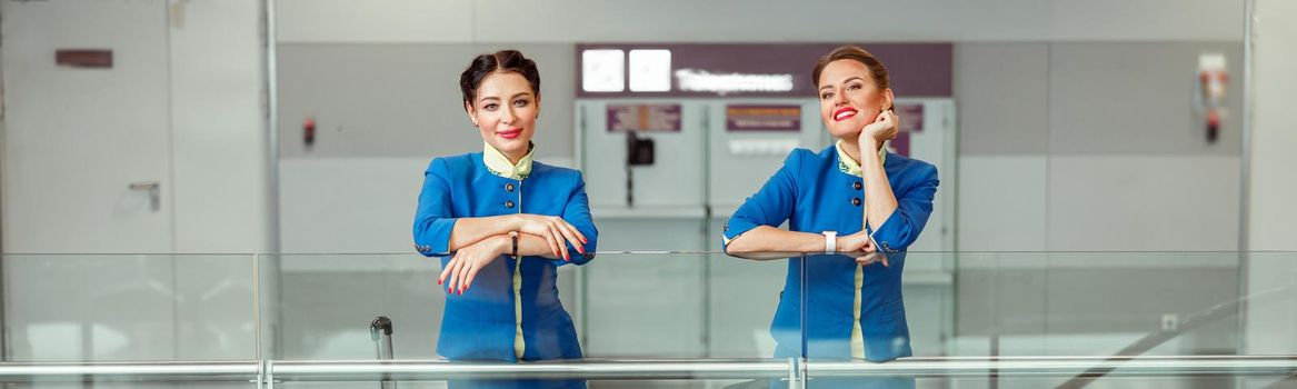 Two women stewardesses with travel bags standing in airport terminal