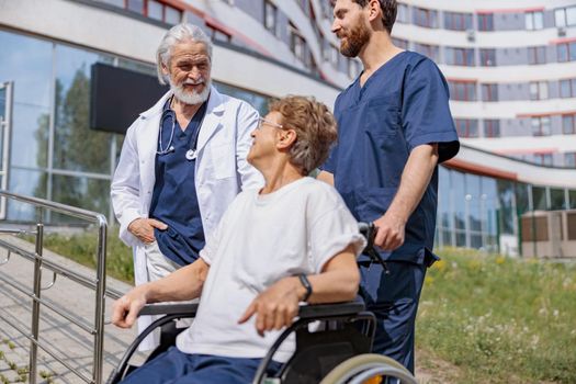 Nurse and doctor talking to patient on wheelchair in hospital yard during walk