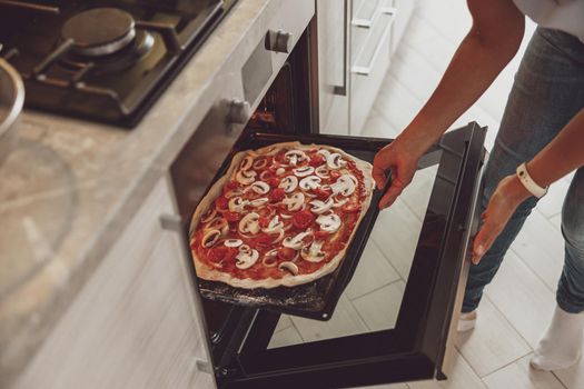 Women's hands put homemade pizza to the oven in modern kitchen