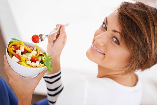 Eating salad with a stunner. Shot of a cheerful young woman eating a salad.
