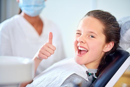 In the hot seat. Portrait of a young girl sitting in a dentists chair giving a thumbs up.
