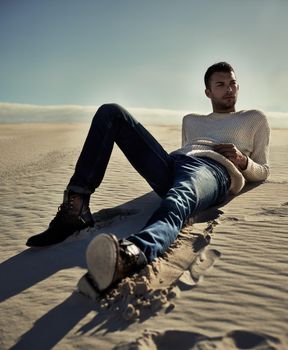 Stylish no matter where he is.... Full length of a handsome male model lying on the desert sand.