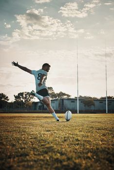 His technique is unmatched. Full length shot of a handsome young rugby player kicking a ball on the field during the day.