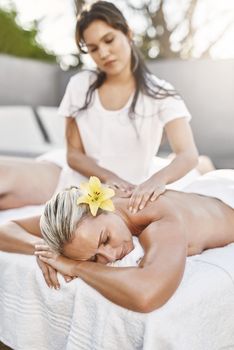 Say goodbye to all of the tension. Shot of a relaxed middle aged woman lying on her stomach while receiving a massage at a spa outside during the day.