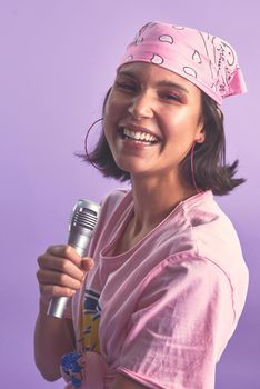 Say hello to the karaoke queen. Studio shot of a beautiful young woman singing with a microphone against a purple background.