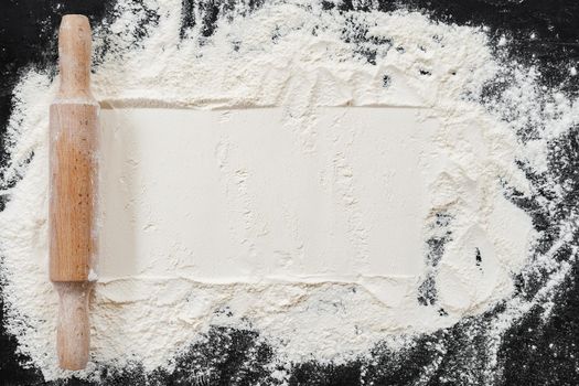 Scattered flour with rolling pin on black background