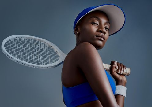 Get up and make it happen. Studio shot of a sporty young woman posing with a tennis racket against a grey background.