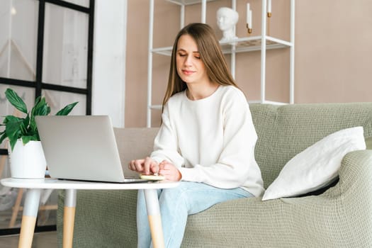Freelance young woman texting with mobile cellphone typing at laptop and working from home office with. Happy girl on workplace at desk. Distance learning online education