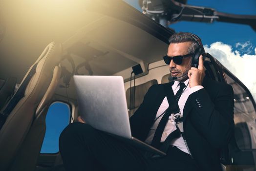 Go anywhere as long as its up. Shot of a mature businessman using a laptop while traveling in a helicopter.