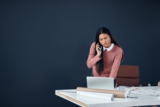 Handling business on all fronts. Shot of an attractive young female architect making a phone call while working in her office.