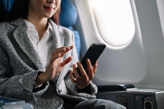 Travel and technology. Young asian woman in plane using smartphone while sitting in airplane seat