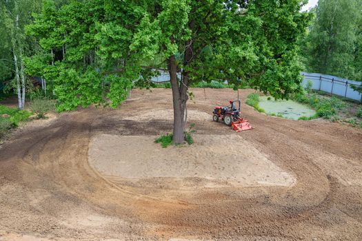 A farmer on a mini tractor loosens the soil for the lawn. Land cultivation, surface leveling