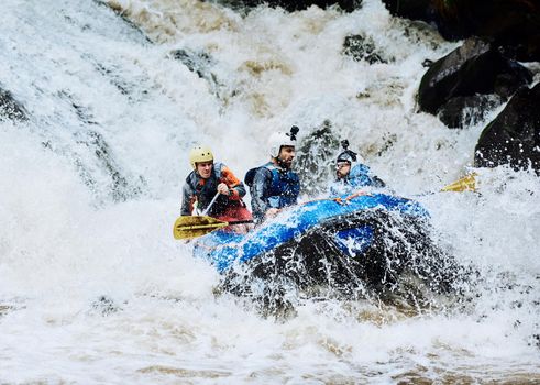 We asked for extreme adventure and we got it. Shot of a group of determined young men on a rubber boat busy paddling on strong river rapids outside during the day.