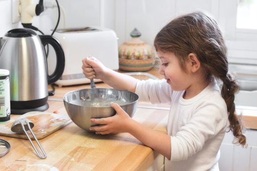 Cute little girl stirring with a whisk and mixing bowl in the kitchen