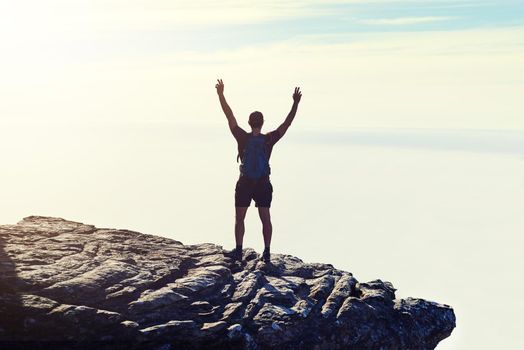 The best view comes after the hardest climb. Rearview shot of an unidentifiable young man raising his arms in triumph on a mountaintop.