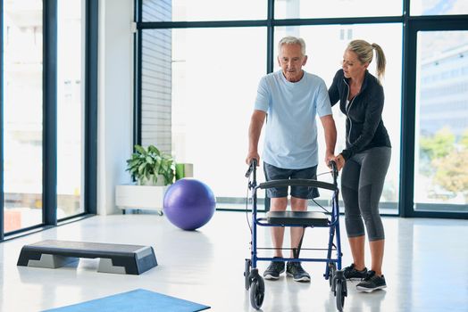 Destination Recovery. Full length shot of a friendly female physiotherapist helping a senior use a walker in a fitness centre.