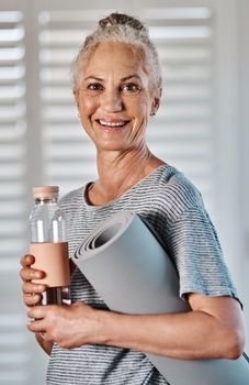 Im ready to get started with the routine. Portrait of a cheerful mature woman holding a bottle of water and yoga mat ready to start her morning session of yoga inside of a studio.