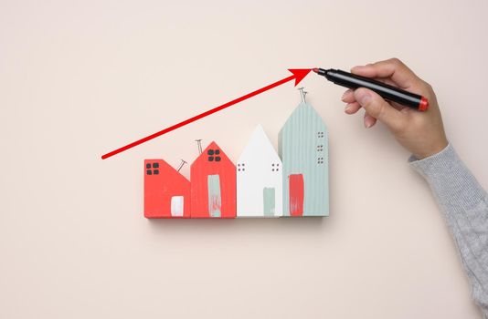 A miniature wooden house and a woman's hand draws a graph with growing indicators.