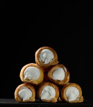 Baked tubules filled with whipped egg whites cream on a black wooden kitchen board