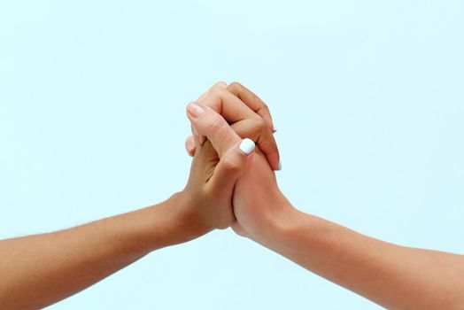 White caucasian female hands and black african american hands hold fingers together in world unity and racial love and understanding in tolerance and racial diversity cooperation concept on blue background.