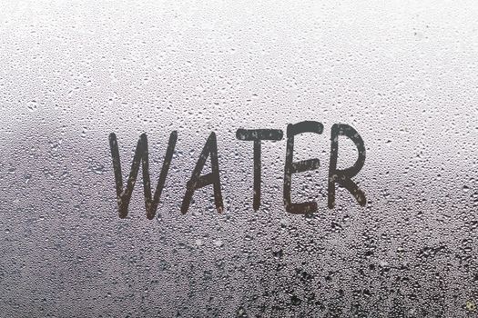 Word water written on foggy window, closeup view