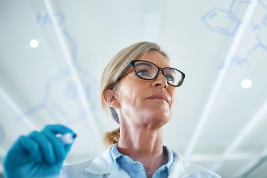 Science is one of the most important channels of knowledge. Shot of a mature scientist drawing molecular structures on a glass wall in a lab.