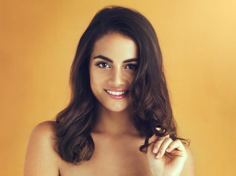 Her most attractive aspect is her alluring smile. Cropped shot of a beautiful young woman playing with her hair against a yellow background.