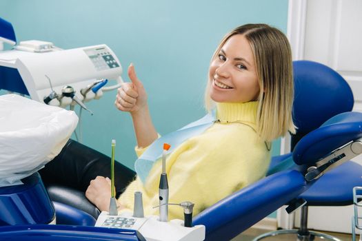 Beautiful girl patient shows the class with her hand while sitting in the Dentist's chair