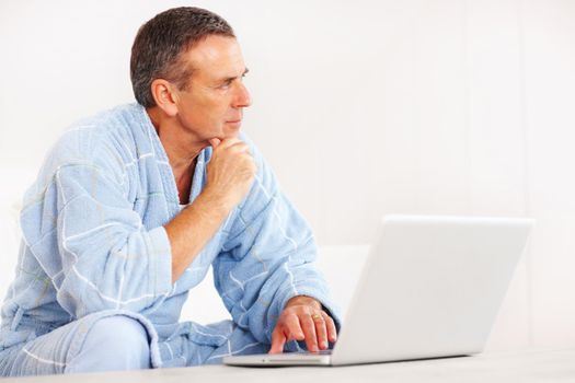 Retired man in bathrobe with laptop looking at copyspace. Portrait of a retired man in bathrobe with laptop looking at copyspace.