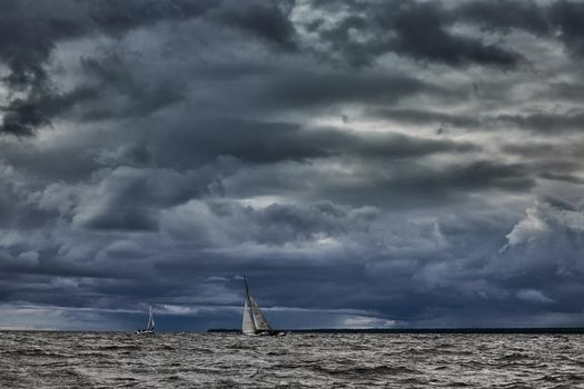 Sailboat in sea at stormy weather, stormy clouds sky orange sky, sail regatta, reflection of sail in the water, bigl waves of water,