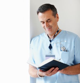 Happy medical doctor noting schedule while leaning against wall. Portrait of a smiling medical doctor noting schedule while leaning against wall.