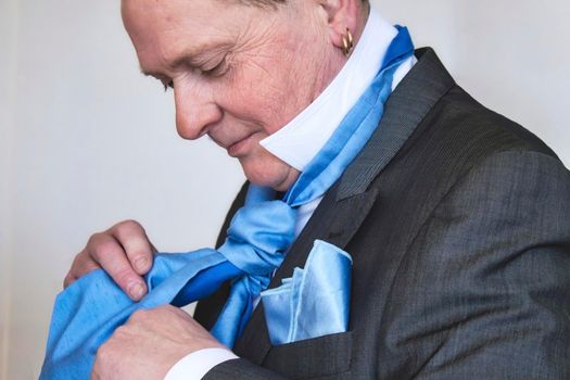 A middle-aged man putting on a silk blue tie dressed in a suit getting ready for a wedding
