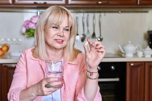 Mature woman holding vitamin pill supplement in her hand and a glass of water