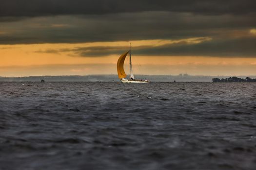 Sailboat in sea at stormy weather, stormy clouds sky orange sky, sail regatta, reflection of sail in the water, bigl waves of water,