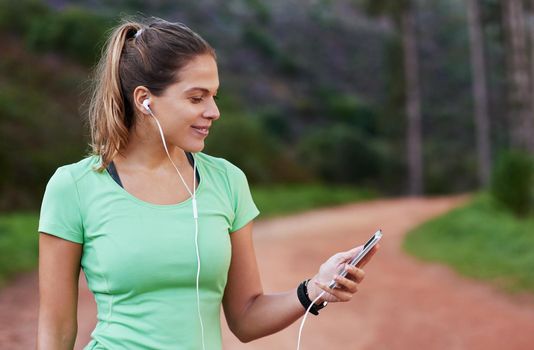 Getting the perfect playlist lined up for her run. Shot of a young woman listening to music while out running.