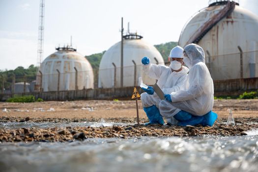 Biologist wear protective suit and mask collects sample of waste water from industry