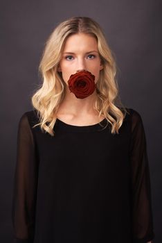 Silenced by love. Conceptual image of a blonde woman with a rose covering her mouth.