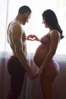 Two hearts, joined as one. Cropped shot of a handsome young man loving his pregnant wife in their bedroom.