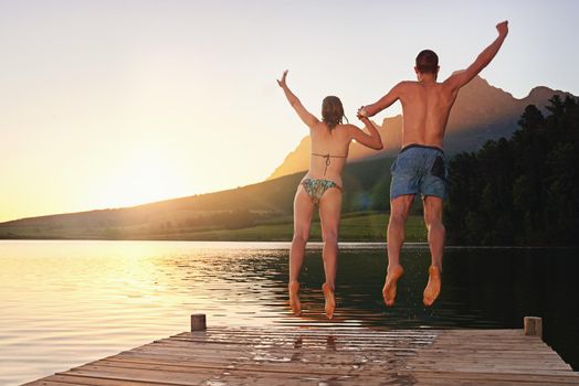 Taking the plunge. Rearview shot of a young couple in swimsuits leaping of a dock at sunset.